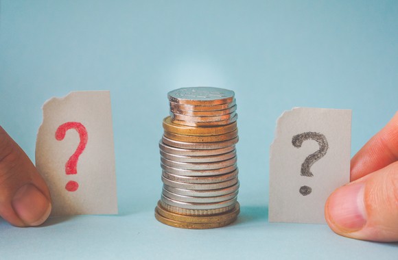 A stack of coins, flanked on either side by fingers holding slips of paper with question marks drawn on them.