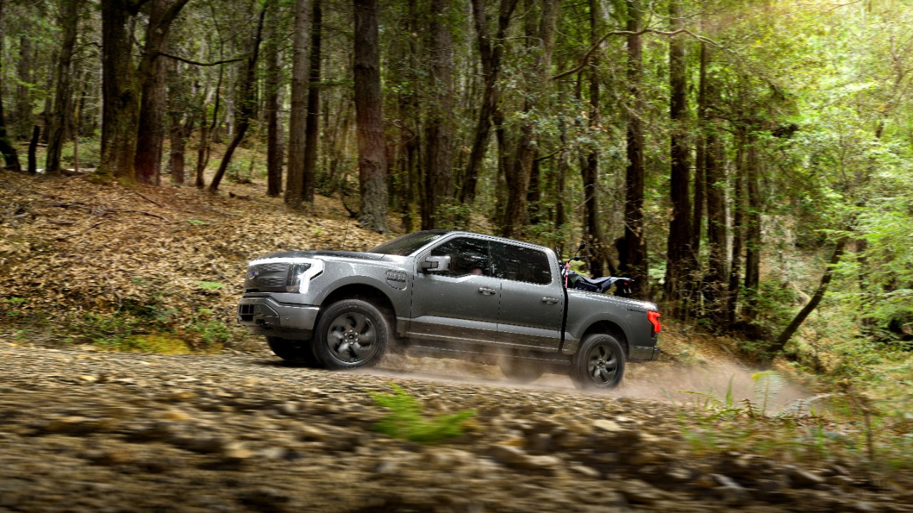 A Ford F-150 Lightning driving in a forest.