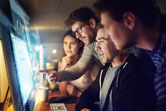 Group of IT workers look at a computer monitor together. 