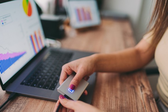 A person holds an external hard drive while working on the computer. 