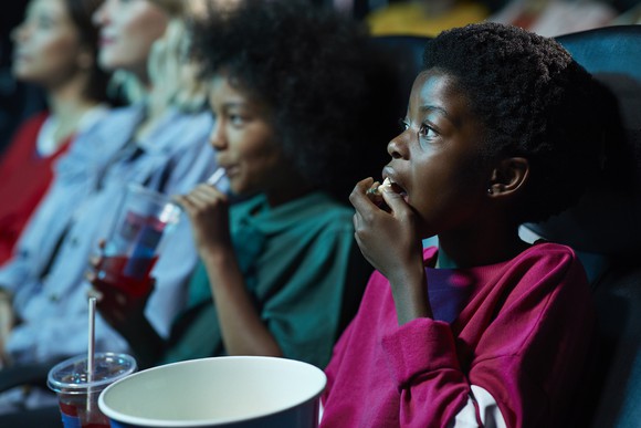 Young siblings watching a movie at a theater while eating popcorn.