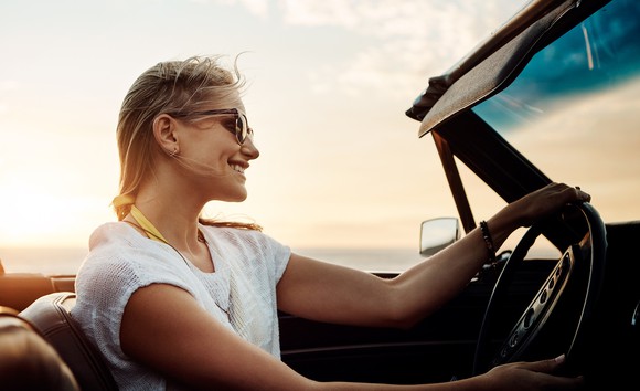 Smiling woman driving convertible as the sun sets in the distance.