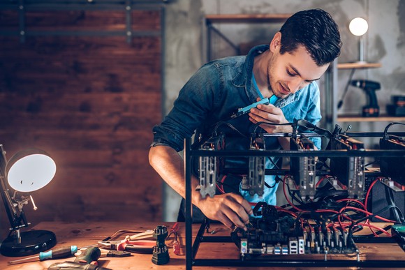 Person working on a cryptocurrency mining rig in a industrial-looking building.