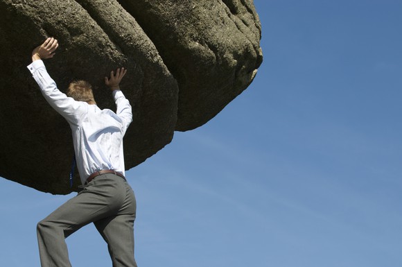 A businessman is pushing a large rock uphill.