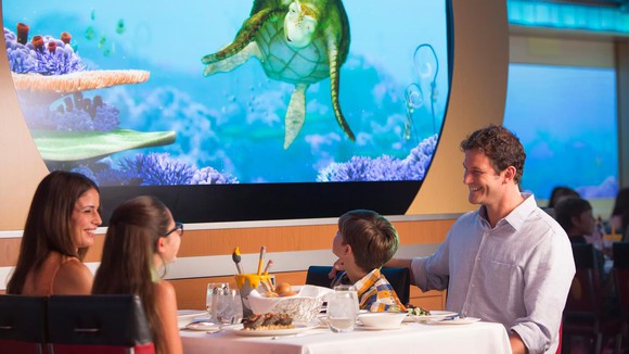 A themed dining room on a Disney cruise ship with sea life projected on the walls.