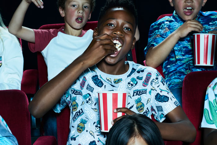 Three young people eating popcorn sitting in movie theater seats.