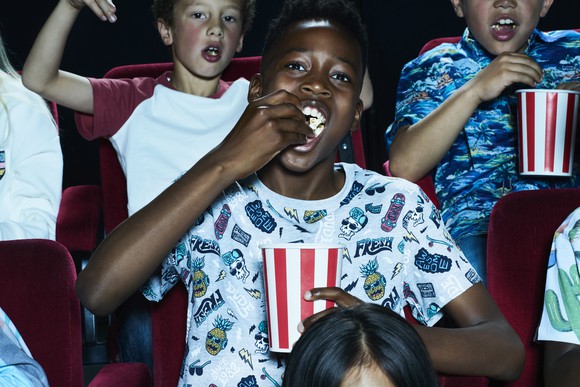 Three young people eating popcorn sitting in movie theater seats.
