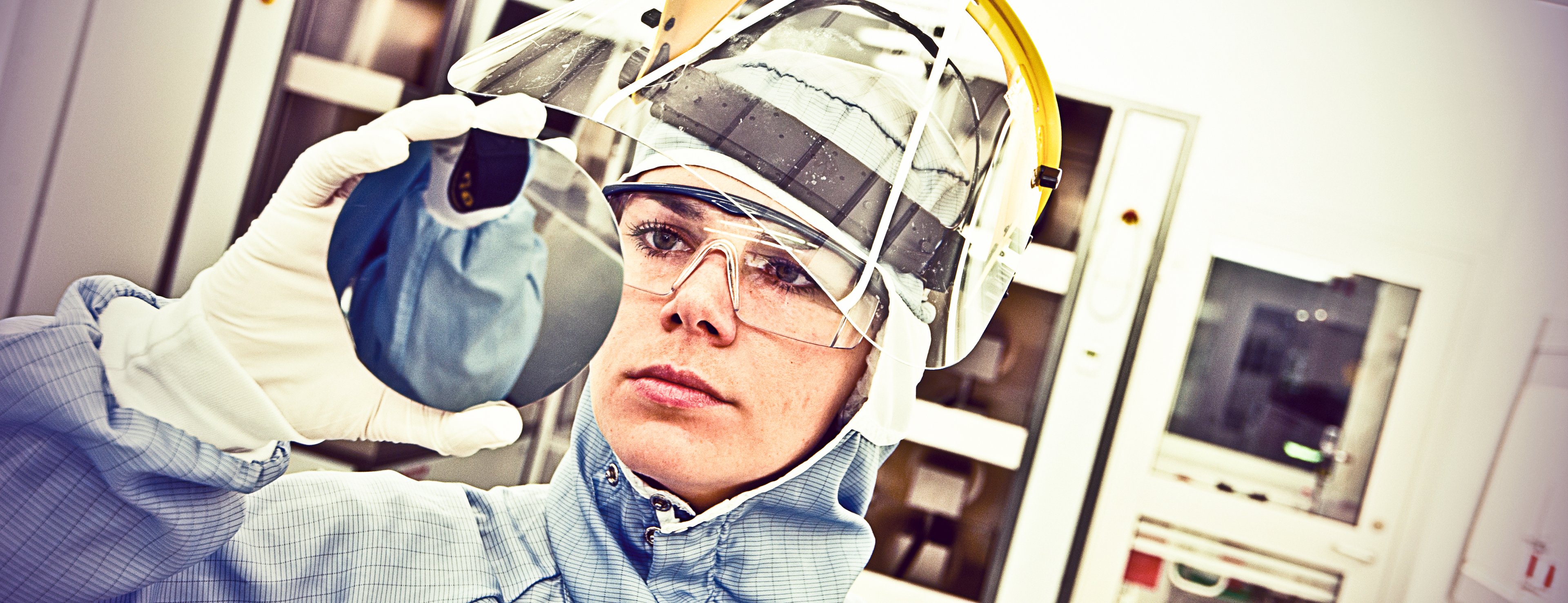 A worker at a fab stares closely at a semiconductor wafer.