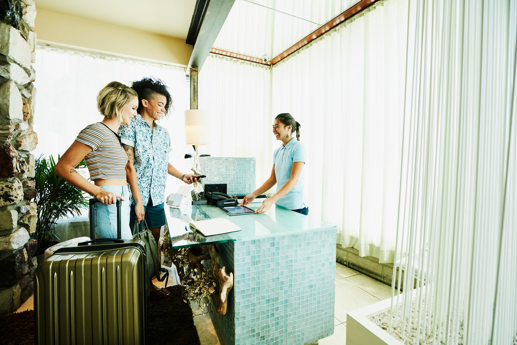 Two travelers with suitcases checking into a hotel with an employee in the lobby.