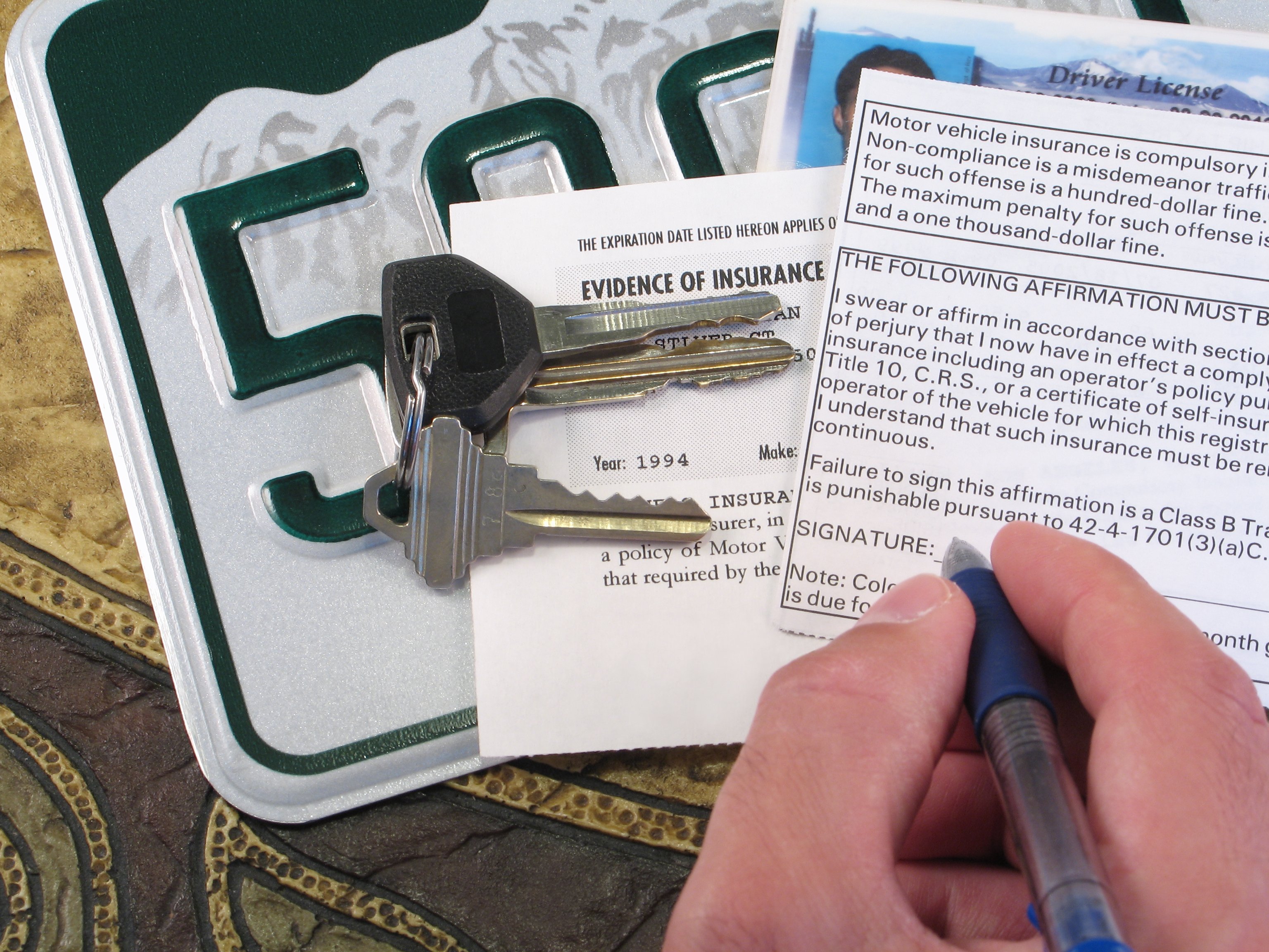 A hand writing on an insurance card with keys sitting on top of a license plate.