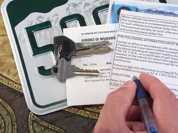 A hand writing on an insurance card with keys sitting on top of a license plate.