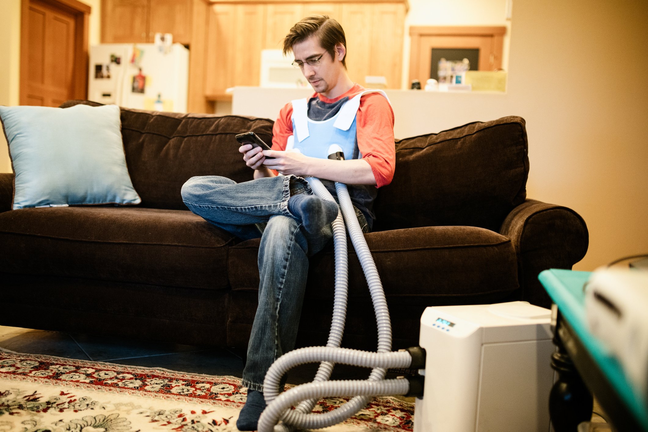 A person sitting on a sofa wearing a  high-frequency chest oscillation system for cystic fibrosis patients.