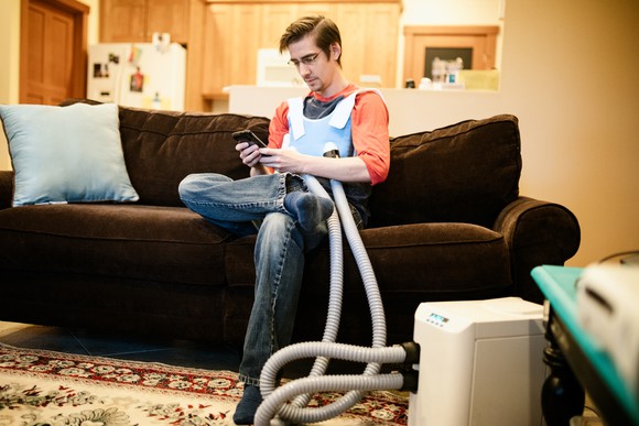 A person sitting on a sofa wearing a  high-frequency chest oscillation system for cystic fibrosis patients.