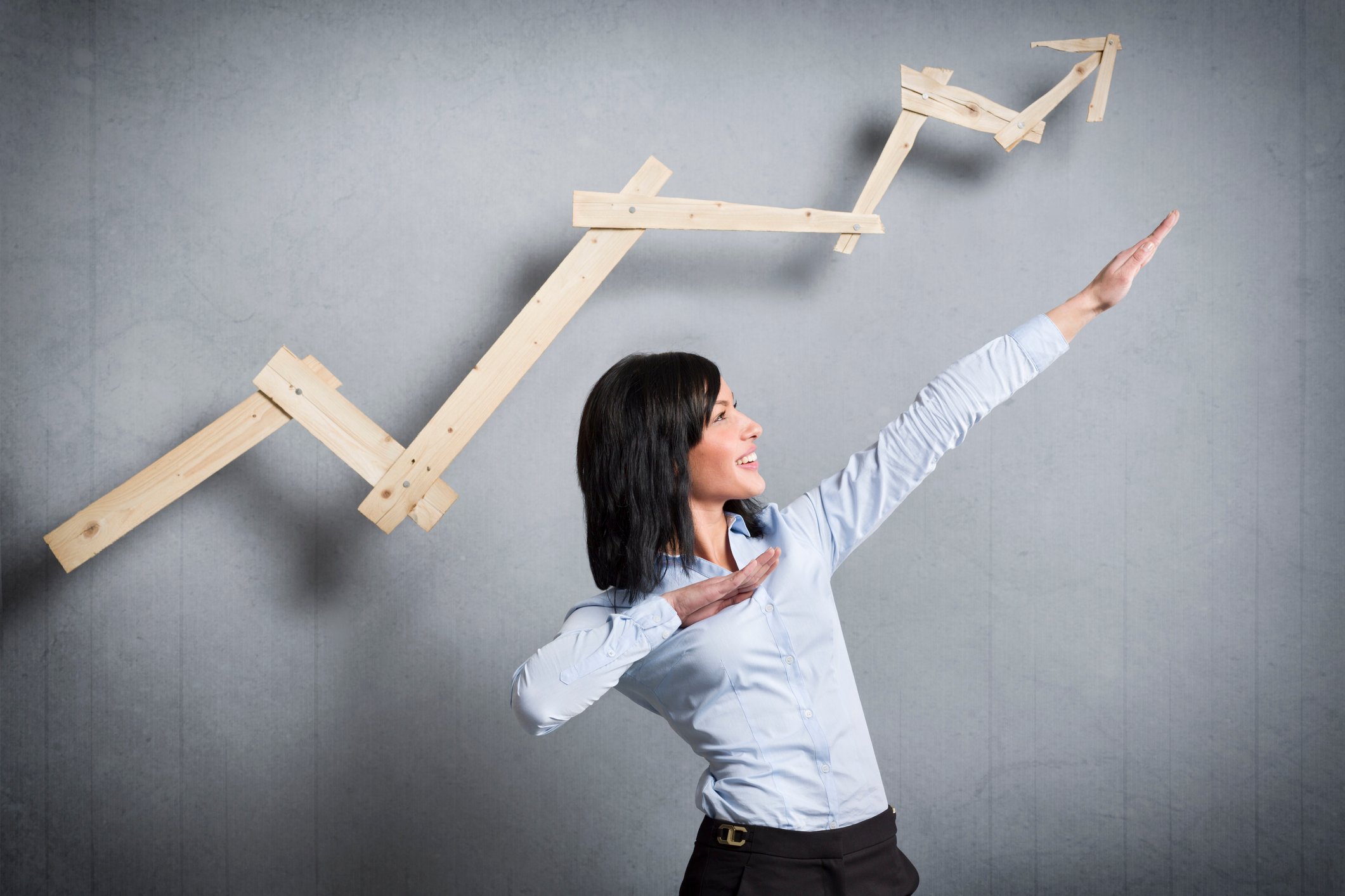 Woman pointing arms upward, below an upward trending arrow.