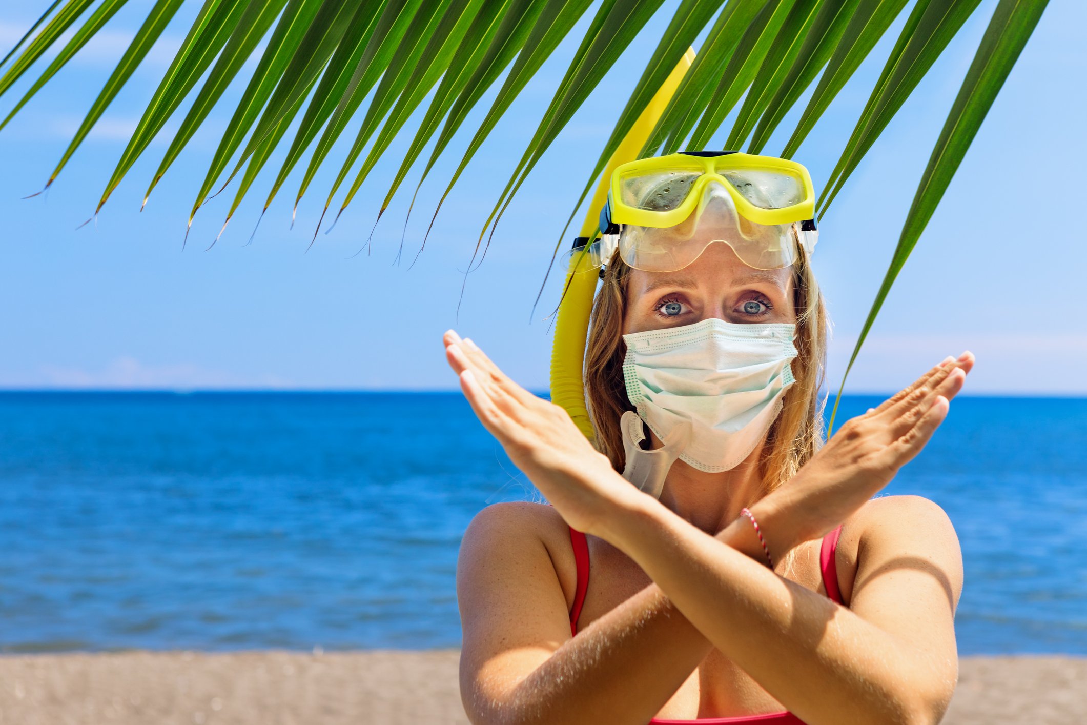 A woman wearing snorkel gear and a face mask makes an X with her arms.