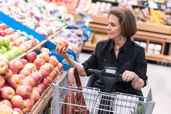 A woman in a motorized wheelchair holding an apple in a grocery store