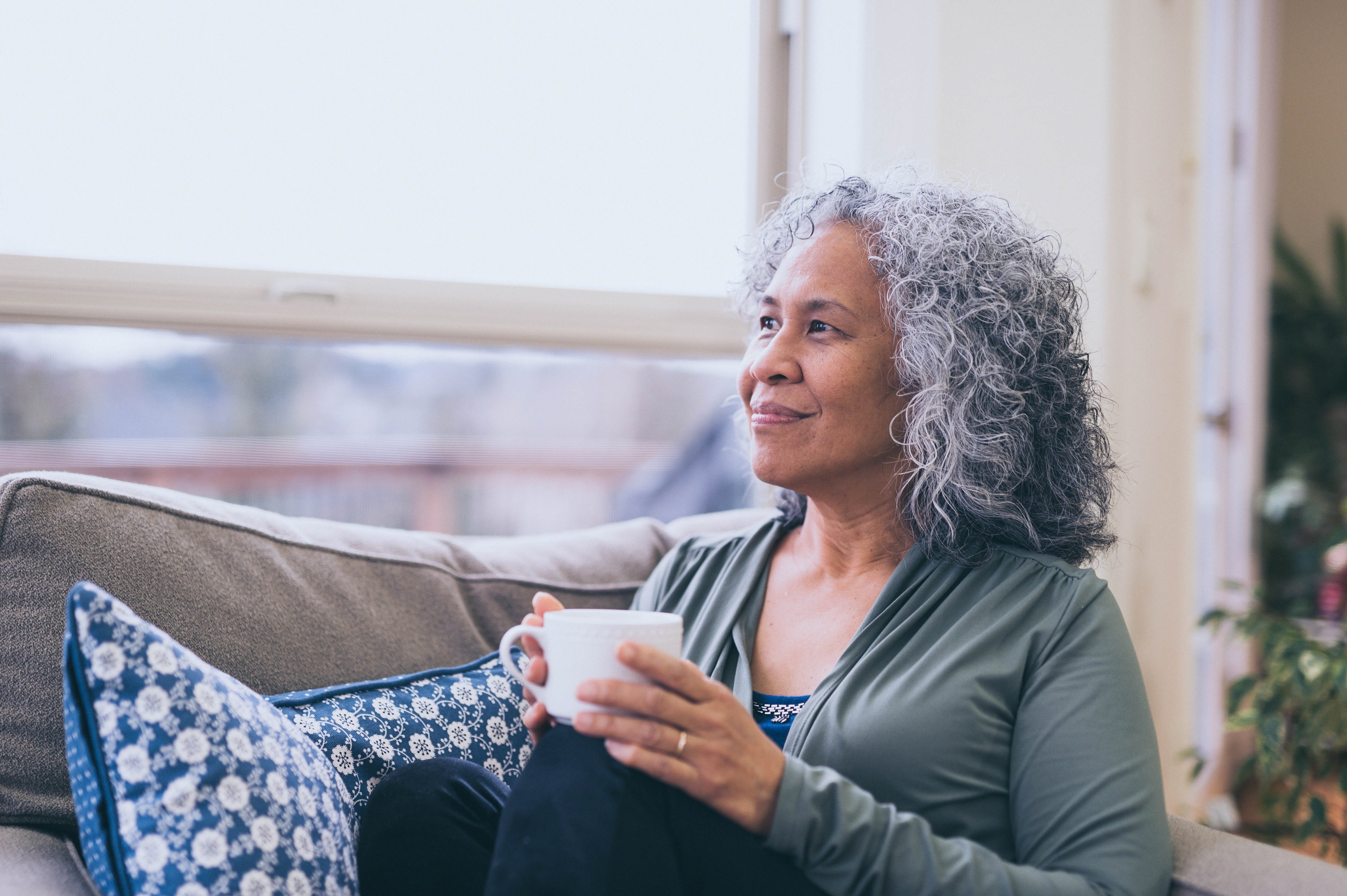A woman holding a mug looks out the window with a smile.