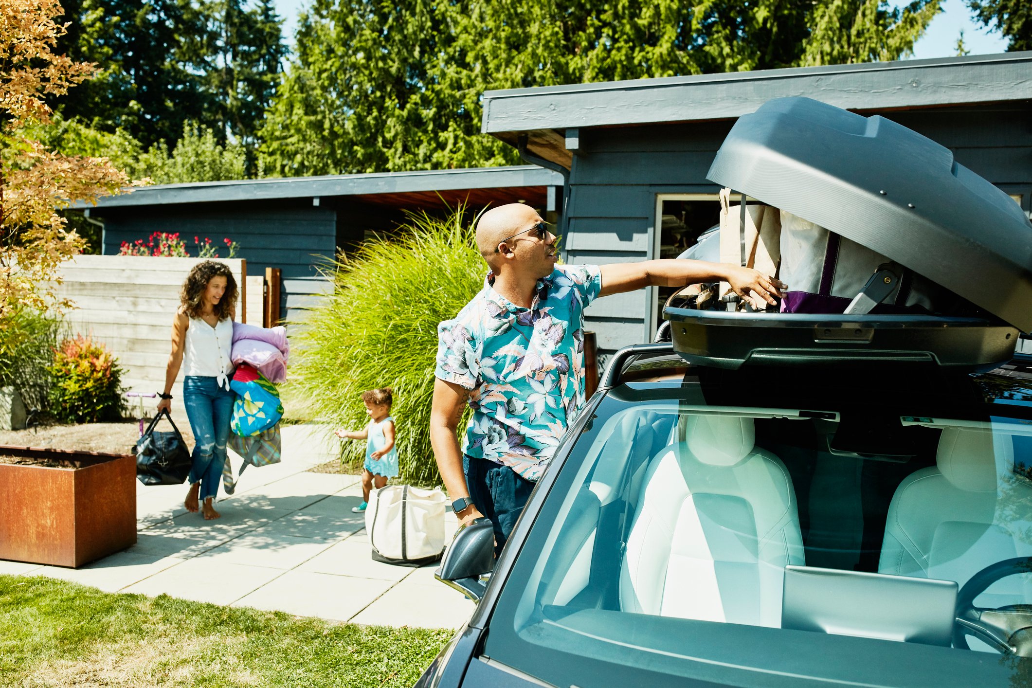 A family loads luggage into a car top carrier in preparation to travel.