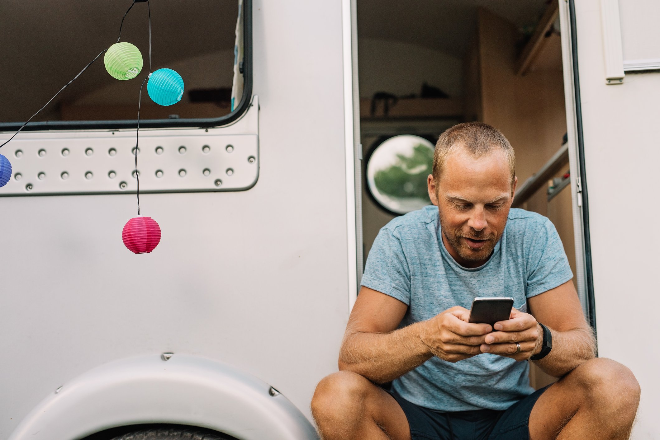 A person sitting outside a recreational vehicle using a mobile phone.
