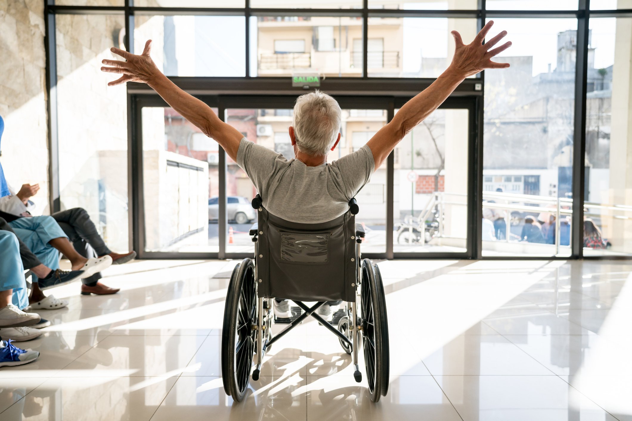 A person sitting in a wheelchair, shown from behind, seems happy, with arms outstretched.
