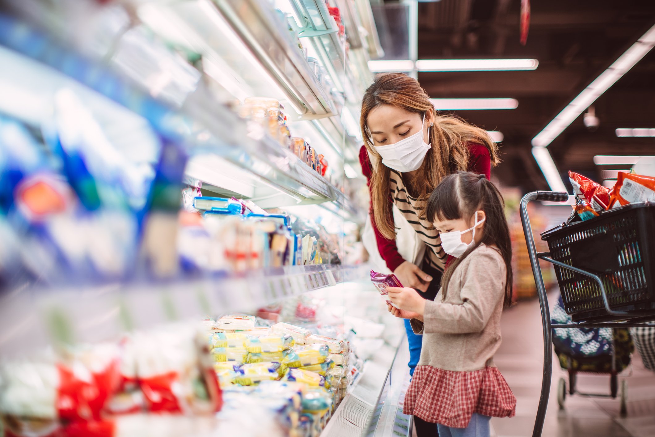 Woman and small girl shopping for groceries while wearing face masks.