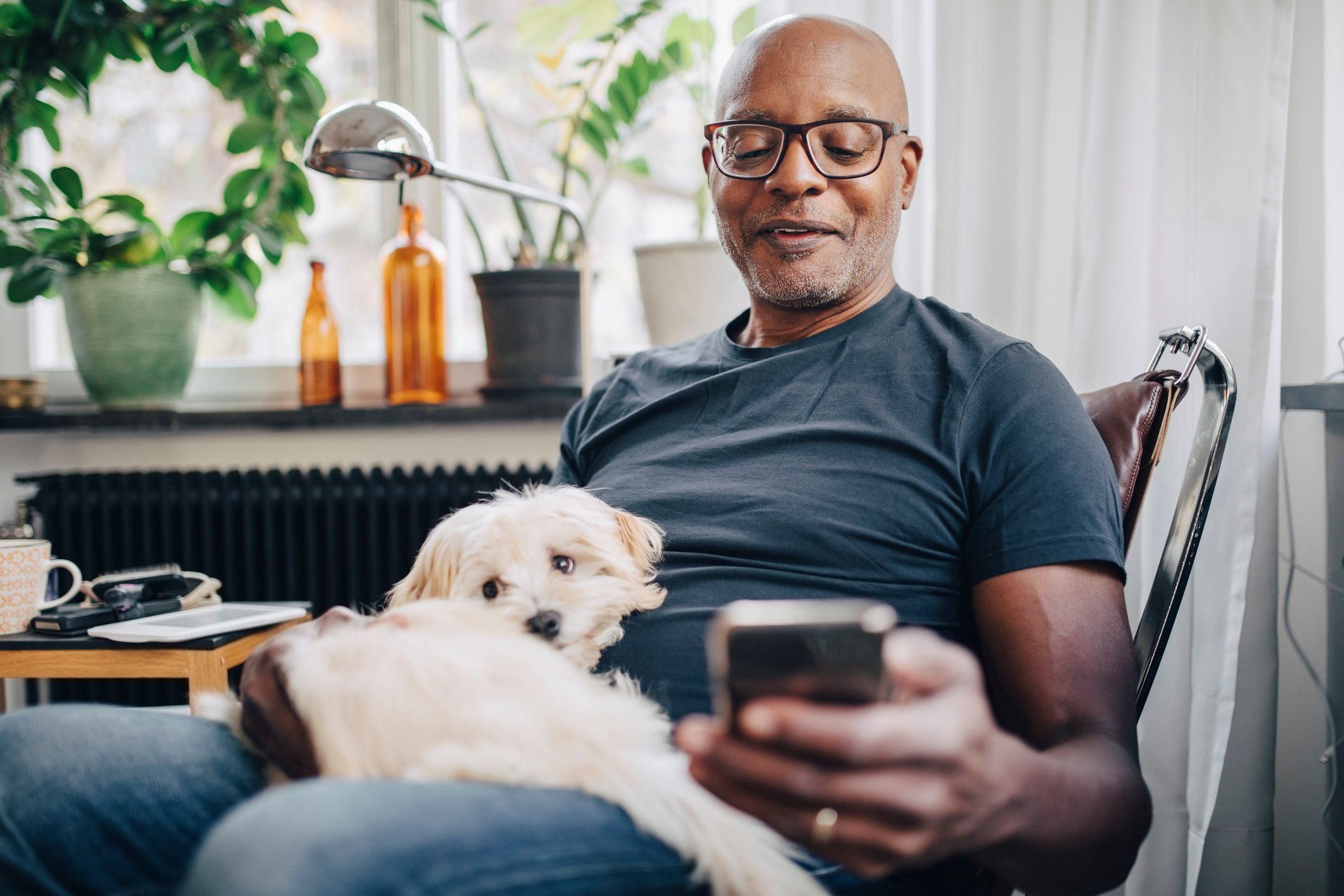 A smartphone user sits with a dog at home.