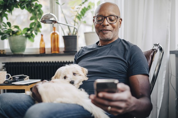 A smartphone user sits with a dog at home.