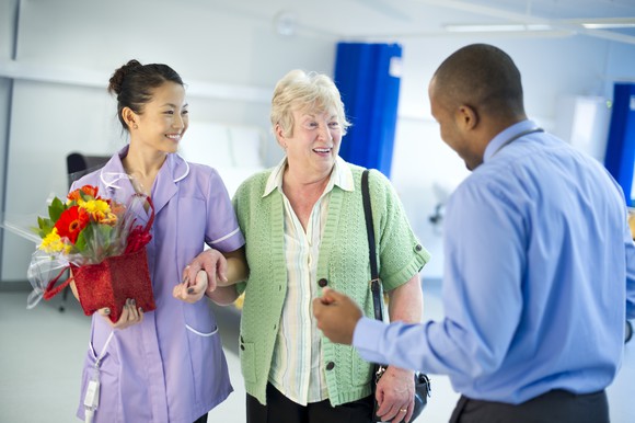 A patient, a nurse holding flowers, and a doctor talking as the patient leaves the hospital unit.