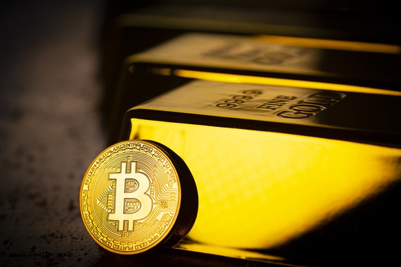 A Bitcoin token leans against a row of gold bullion bars.