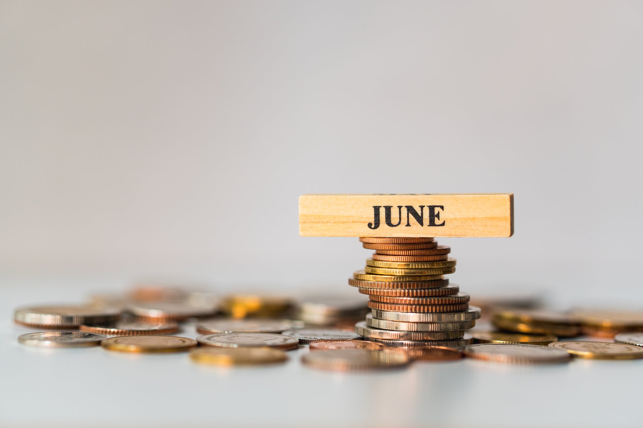 A wooden block that reads "June" sits on top of a pile of coins.