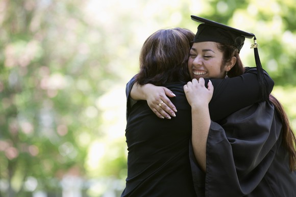 A woman in cap and gown hugging her mom.
