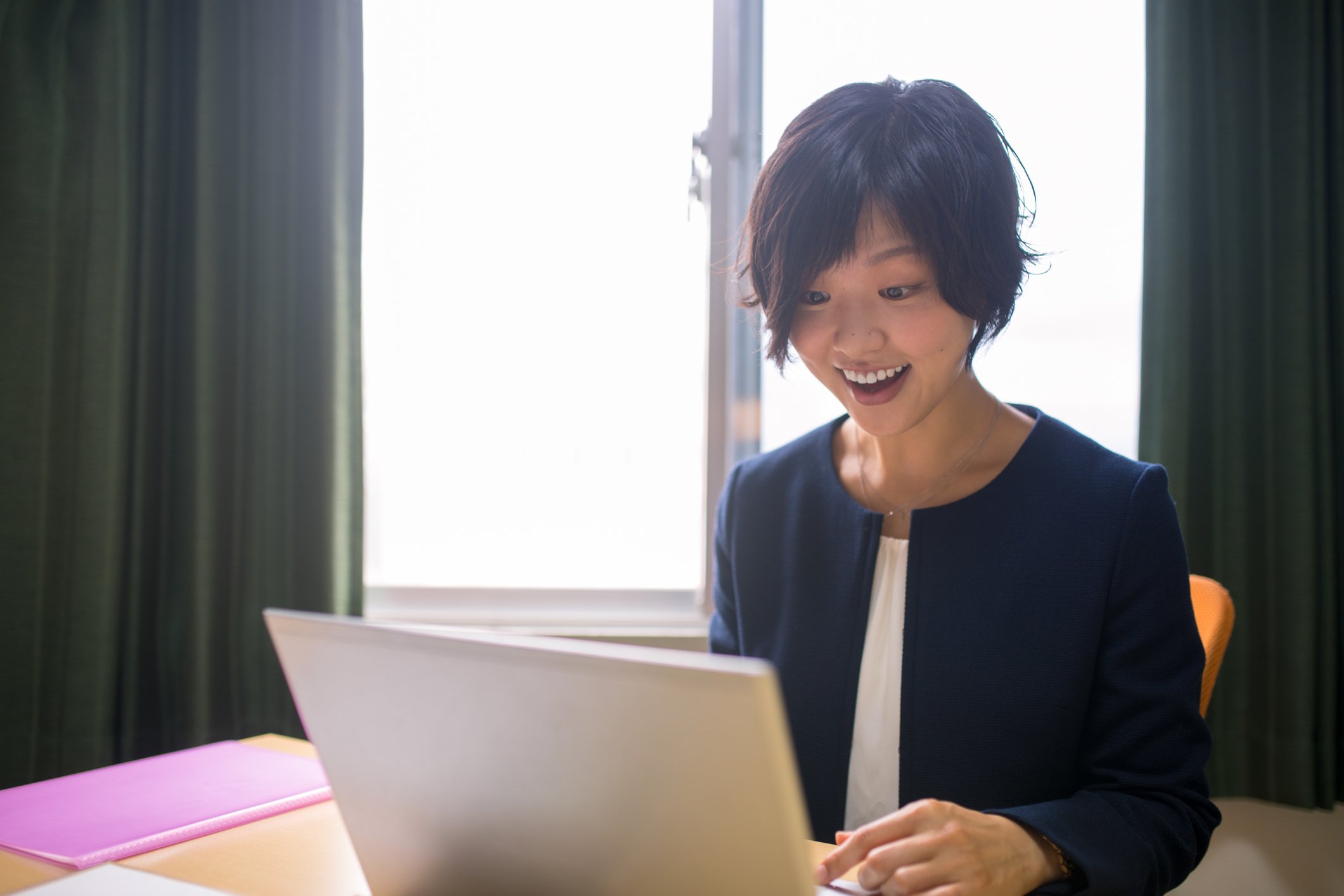 A person looks pleasantly surprised at what they see on the screen of their laptop.