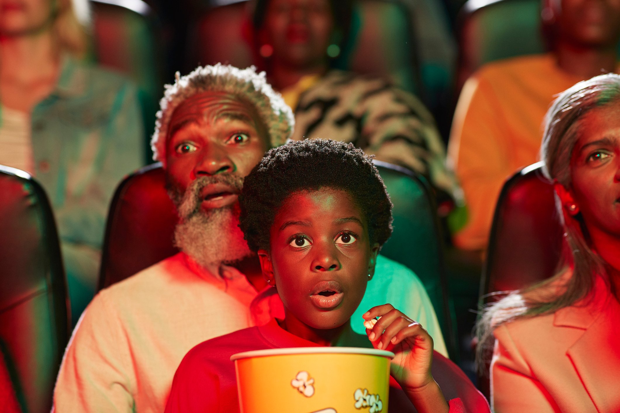 A grandfather and young grandchild on his lap watch a movie in a theater. 