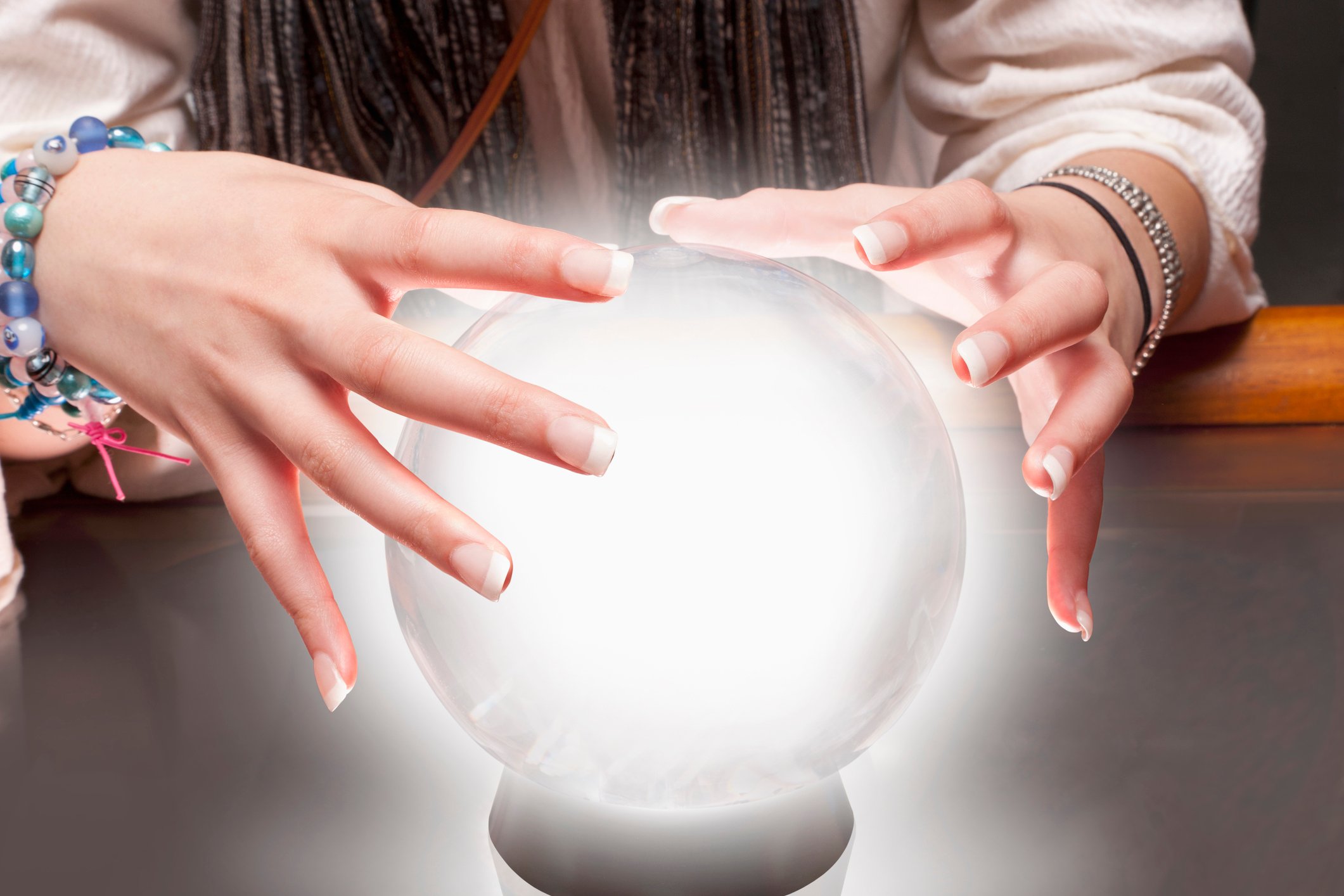 Two hands hovering over a crystal ball that is lighting up.