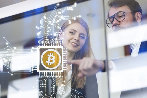 Two executives look at a clear board with a Bitcoin symbol on it. 