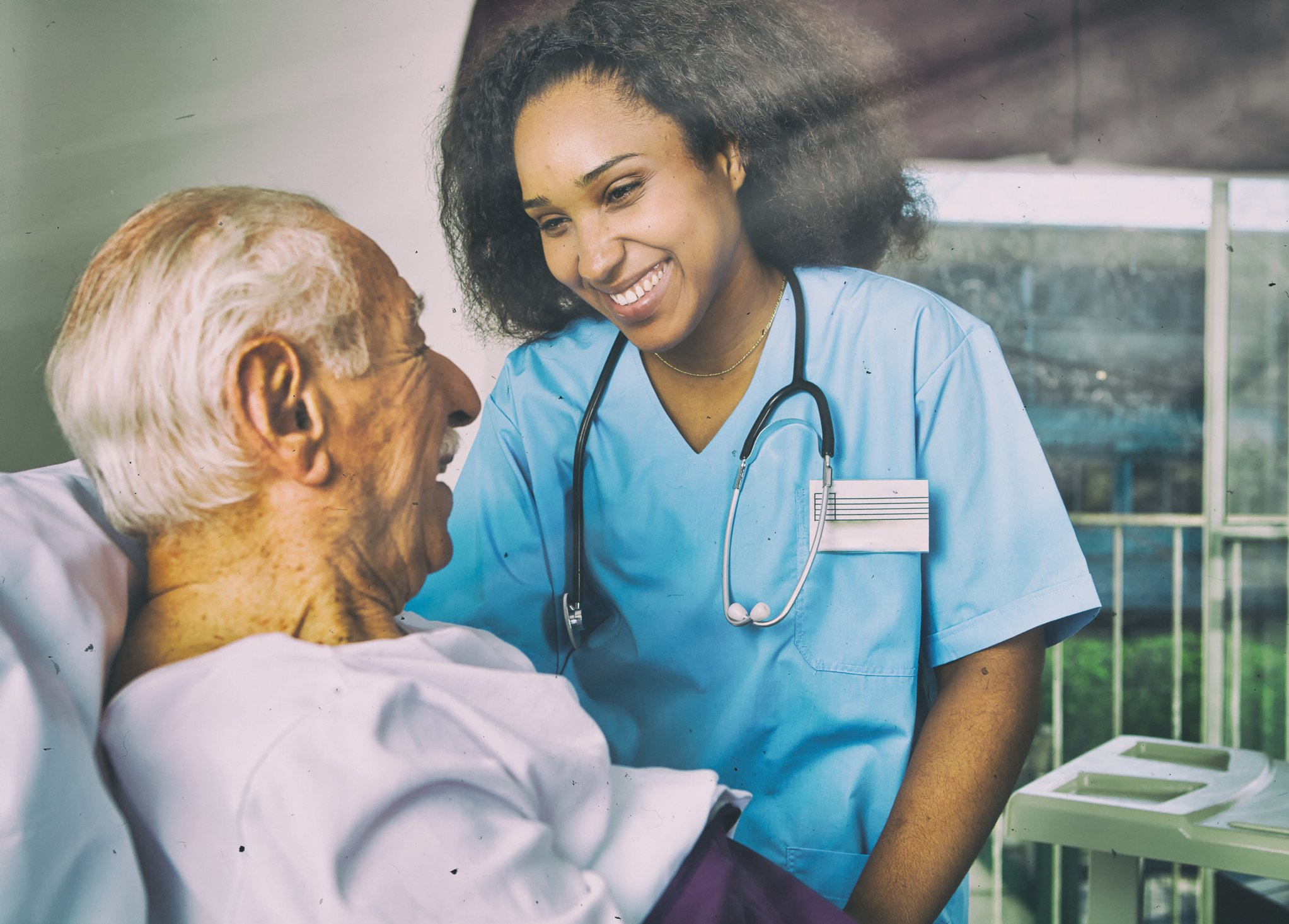 A smiling nurse caring for an elderly patient i na hospital bed.