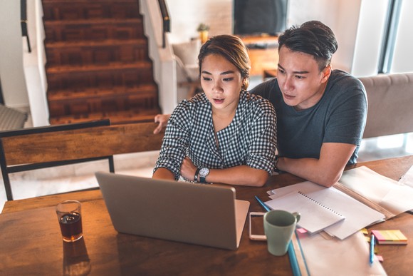A young couple sitting at a table with pieces of paper and a laptop sitting in front of them.