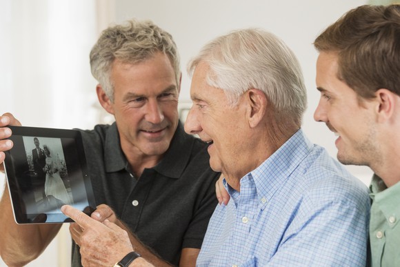 Two family members show an older person a wedding photo on a tablet.