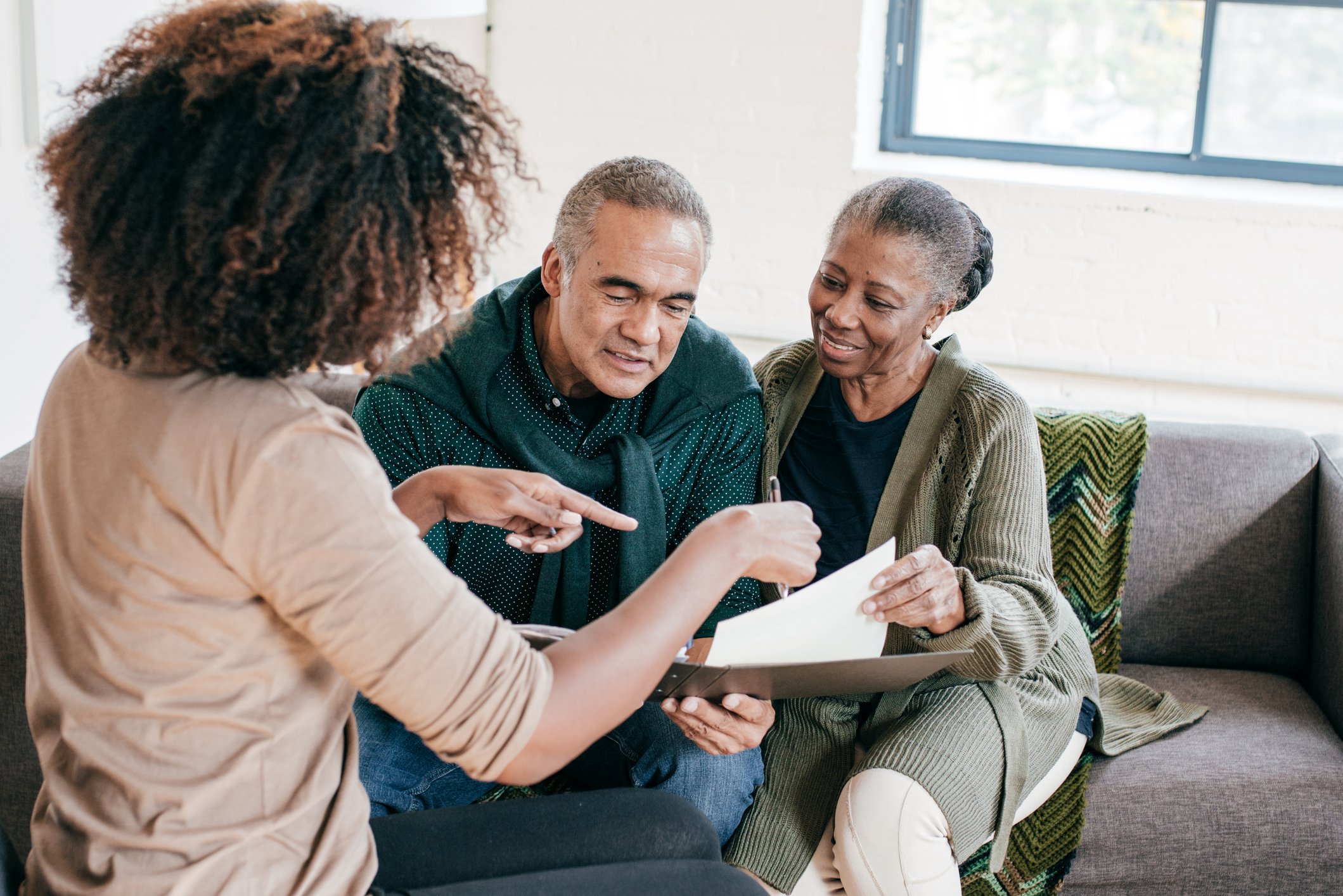 A person explaining insurance forms to an older couple seated on a sofa.