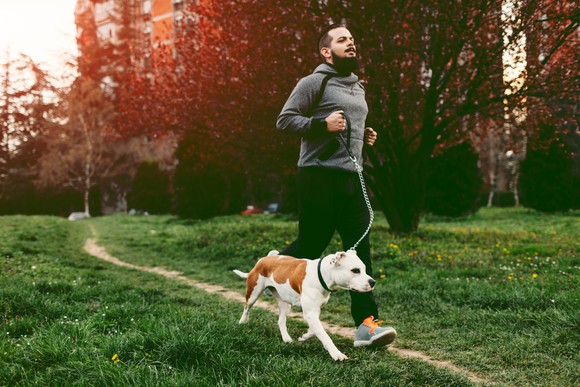 A person wearing athletic wear and running outside with a dog.