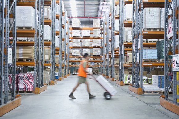 A warehouse worker pushes a dolly down a long aisle.