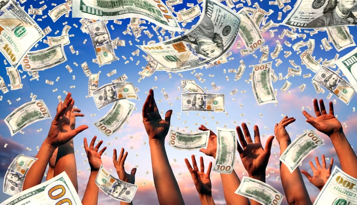 Hands reaching up as $100 bills fall from sky.