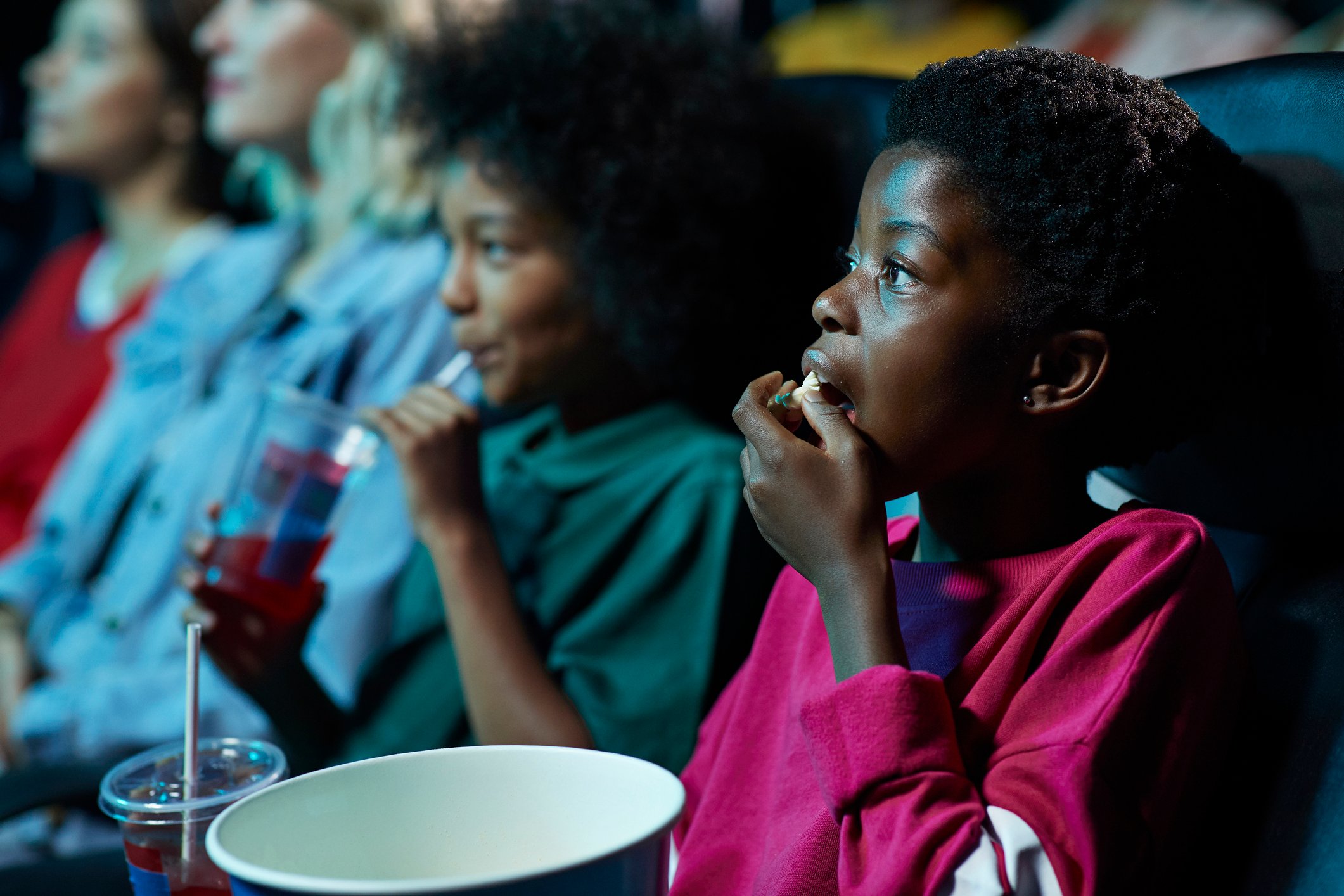 Kids eating popcorn inside a movie theater while watching a movie. 