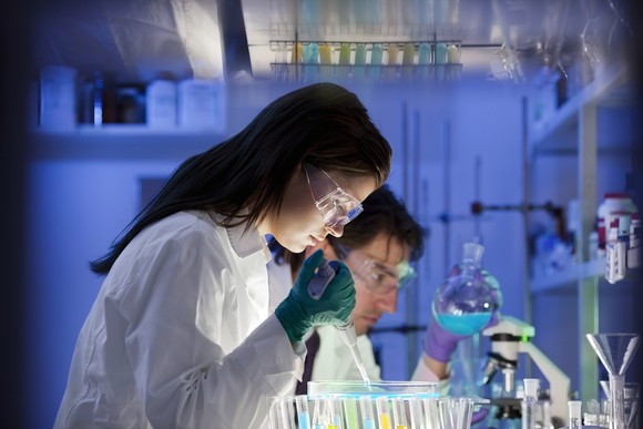 Lab workers with goggles are looking at samples in test tubes.
