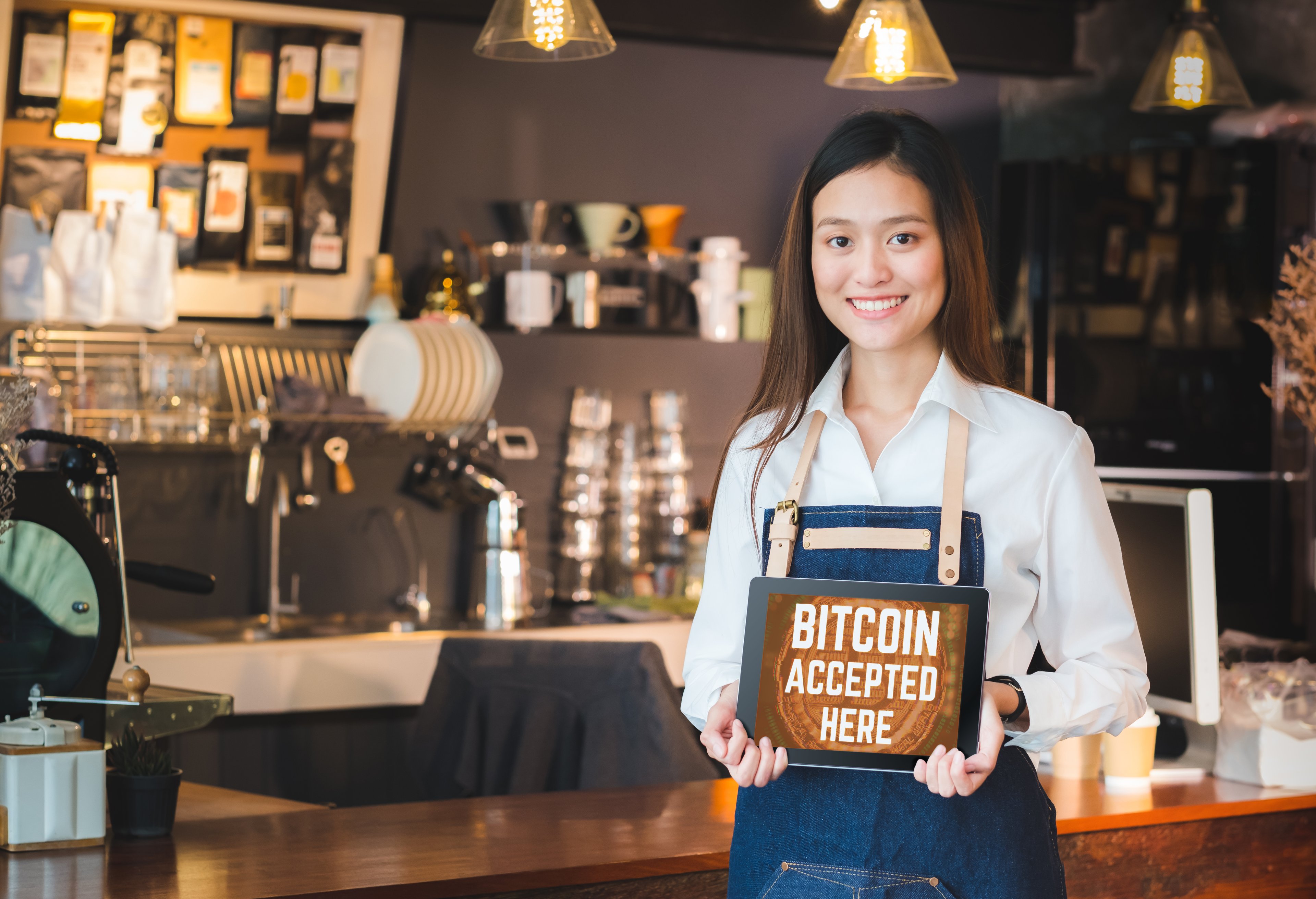 Someone in a coffee shop holding a tablet that displays the message "Bitcoin accepted here."