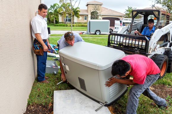 Several workers moving a generator into position near a home.