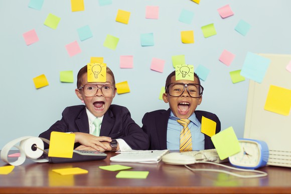 Two children dressed as businessmen play with sticky notes.