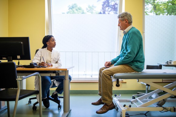 A doctor, seated in front of a computer, looks at a patient answering questions.