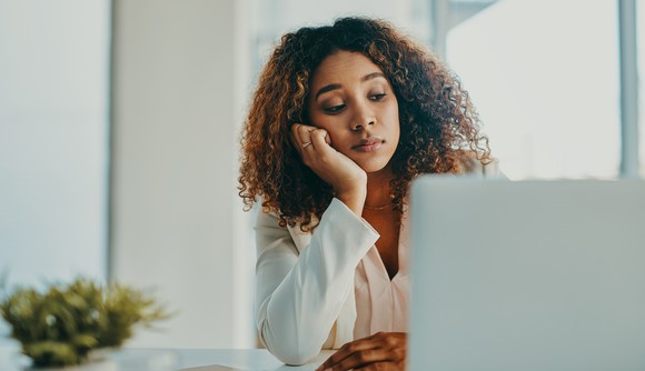 A woman, sitting at her laptop with her hand on her chin, looking concerned. 