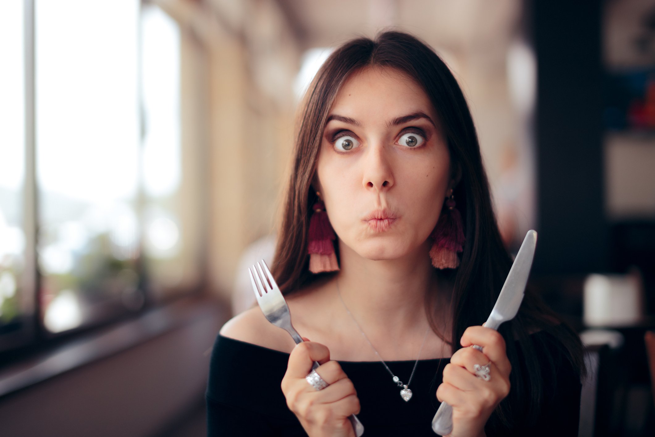 A person in a restaurant holding a fork and knife.